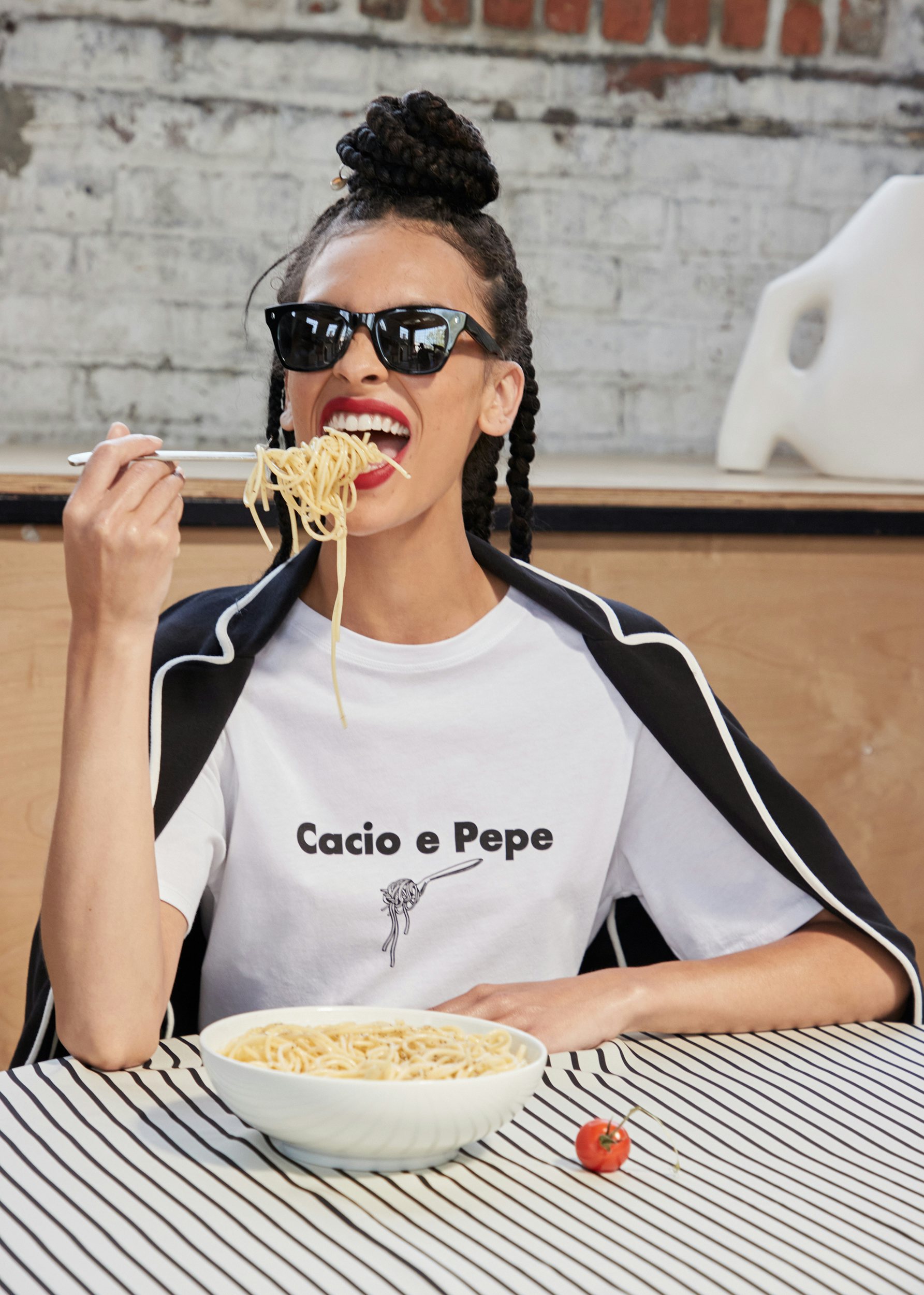 A KULE model having fun eating Cacio e Pepe. She is wearing our new Modern White Cacio e Pepe printed/graphic tee. Layered on top is the new Syd Jacket in black. She is sporting black sunglasses. Hungry for Italian anyone?