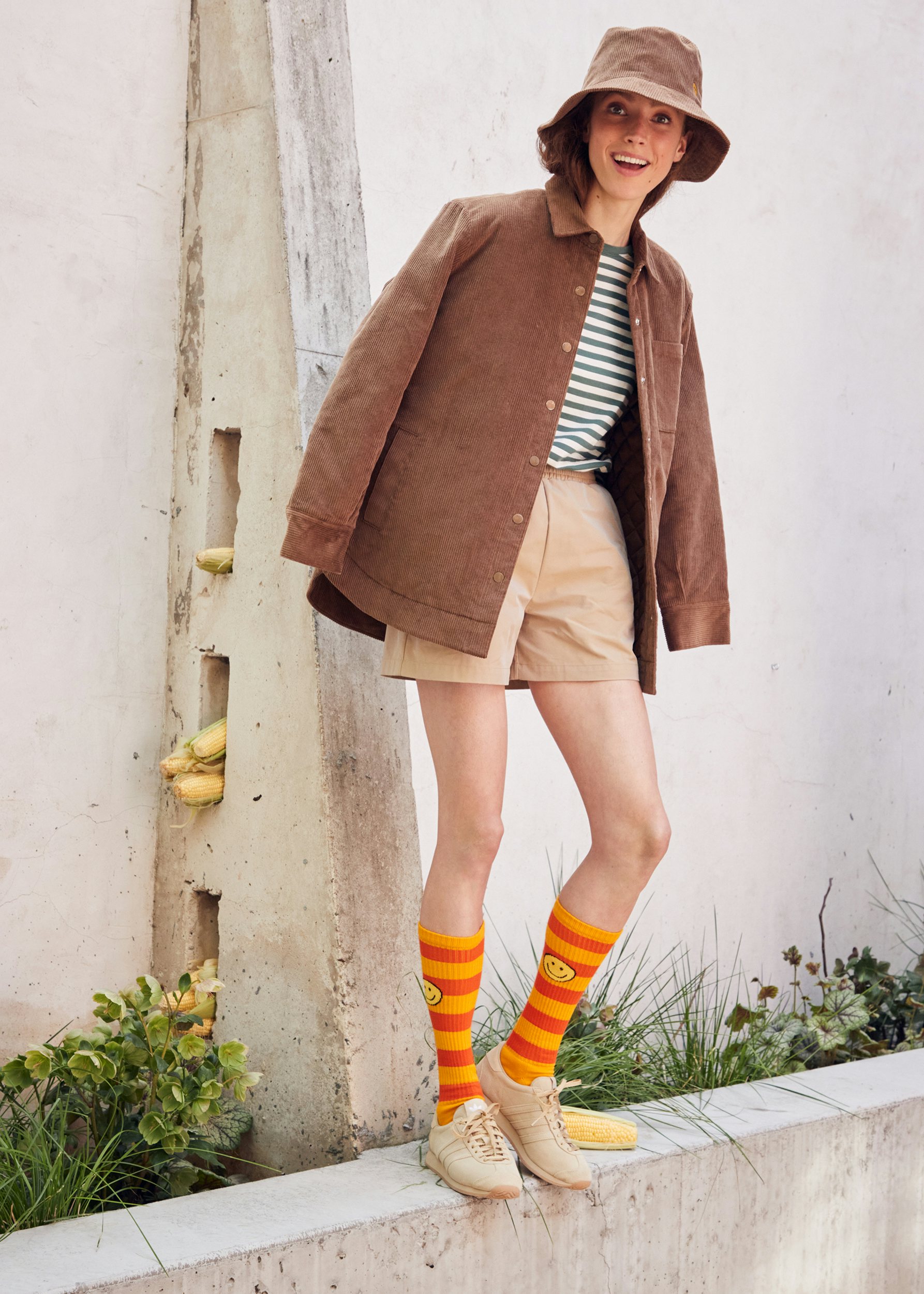 Model wearing the new KULE Bucket Hat in corduroy khaki, paired with the new Dante outerwear jacket in the new fall color, latte. She is also sporting khaki shorts (not sold at KULE), a Modern Long tee in Forest/Cream, and knee-high rugby socks in Gold/Poppy.