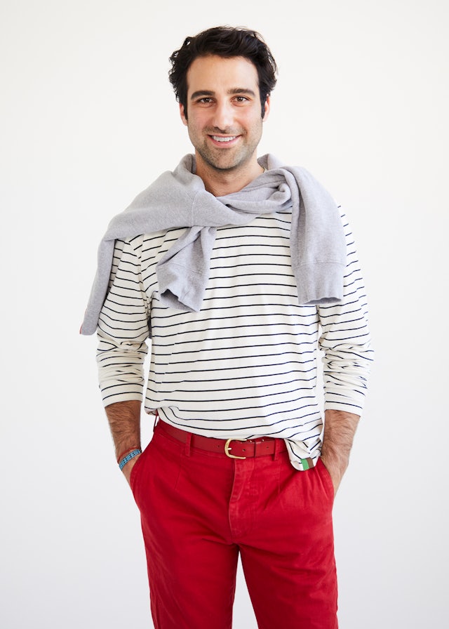KULE Green - Closeup of model wearing the Rufus organic cotton stripe tee with a sweatshirt tied around his neck and red pants.